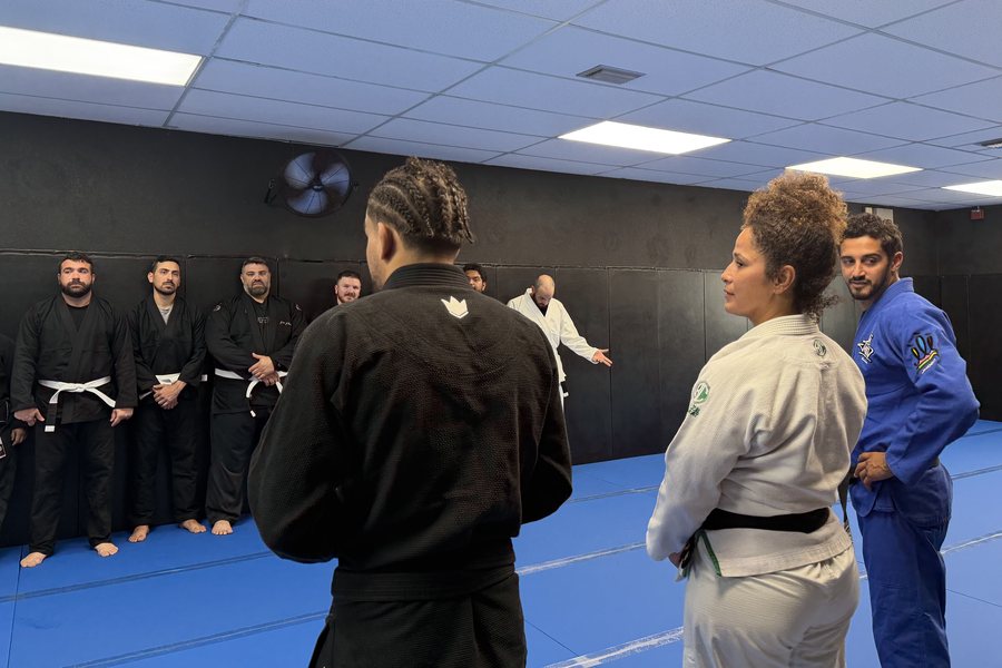 Adult class lined up along the wall while an instructor demonstrates a technique
